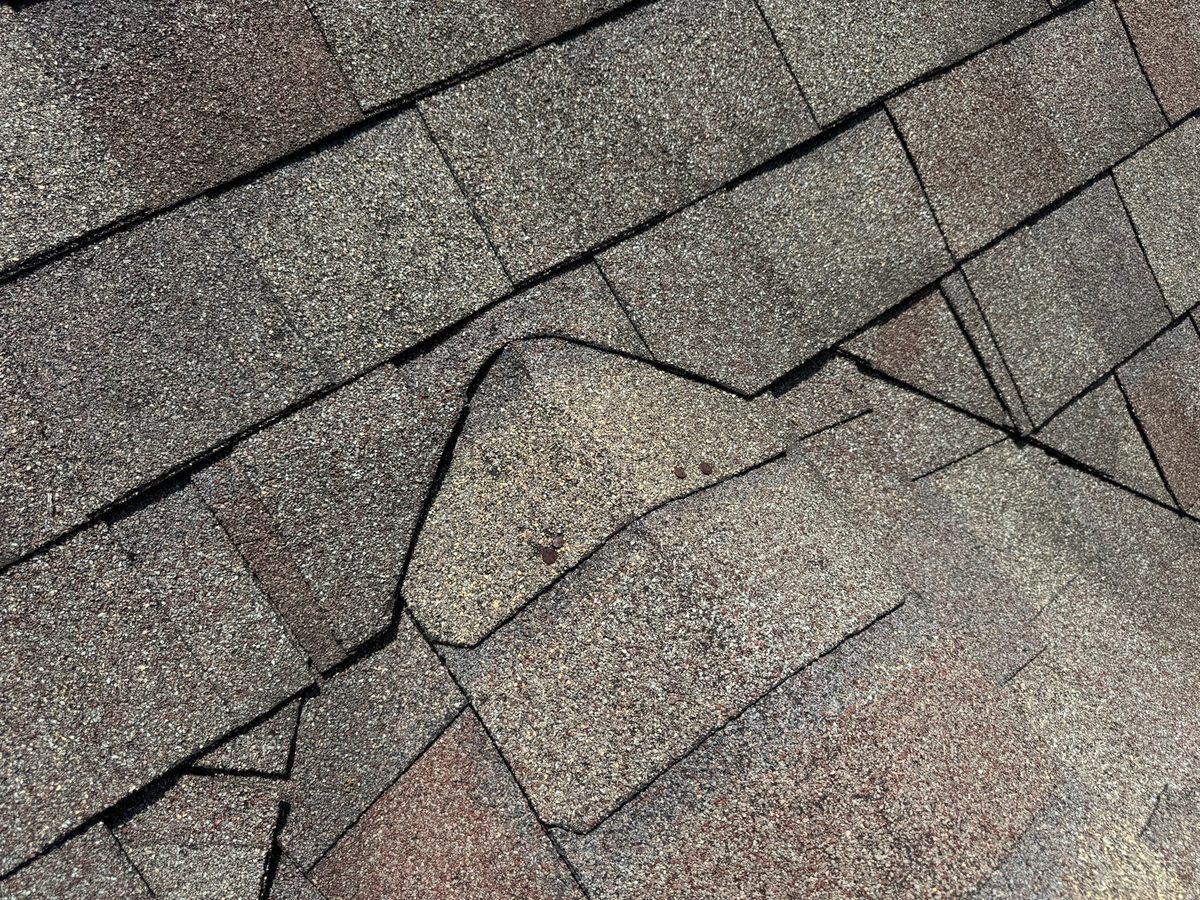 Cracked and displaced shingles on an asphalt roof found during a home inspection in Gladstone, MO