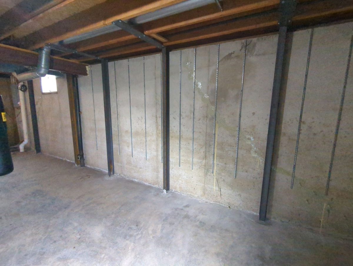 Steel wall braces from a prior foundation repair on a poured concrete basement wall found during a home inspection in Grandview, MO