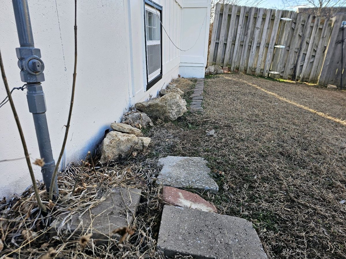 Negative grading with soil and landscape rock sloping toward the foundation found during a home inspection in Grandview, MO