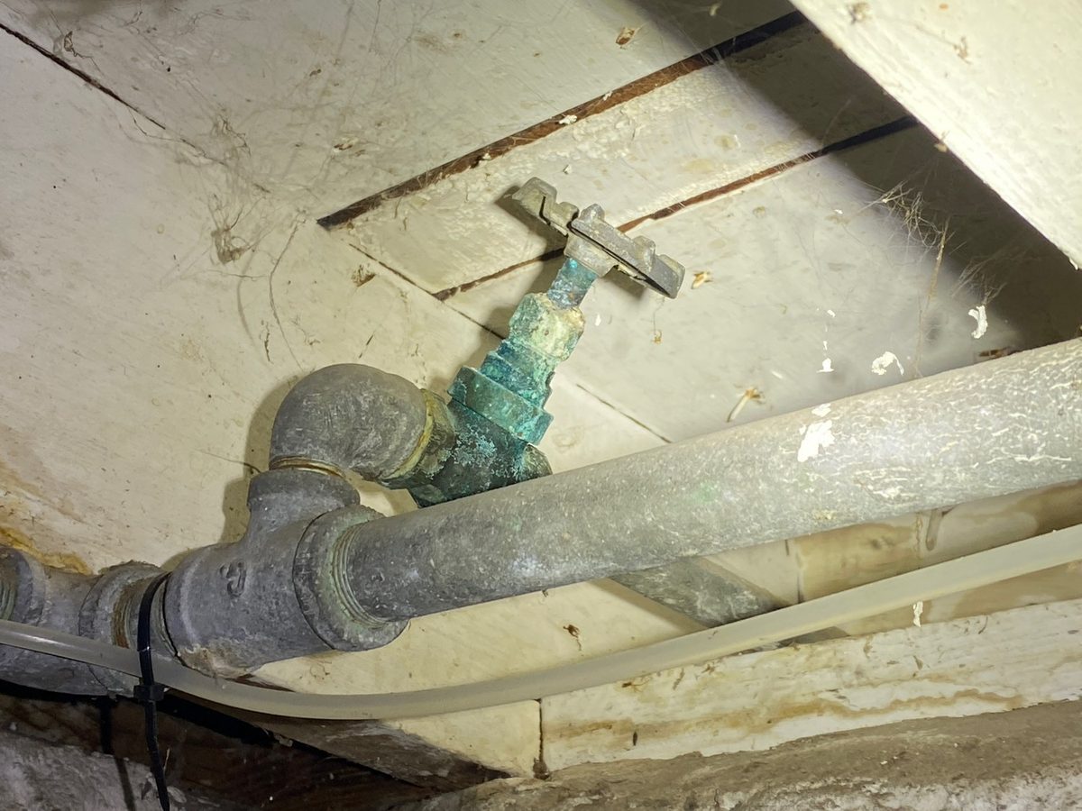 Galvanized water supply pipe with heavy corrosion on a shutoff valve under wood floor framing