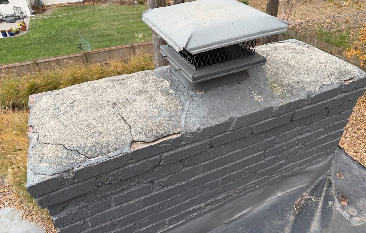 Cracked and deteriorating masonry chimney crown around a metal chimney cap found during a home inspection in Leawood, KS