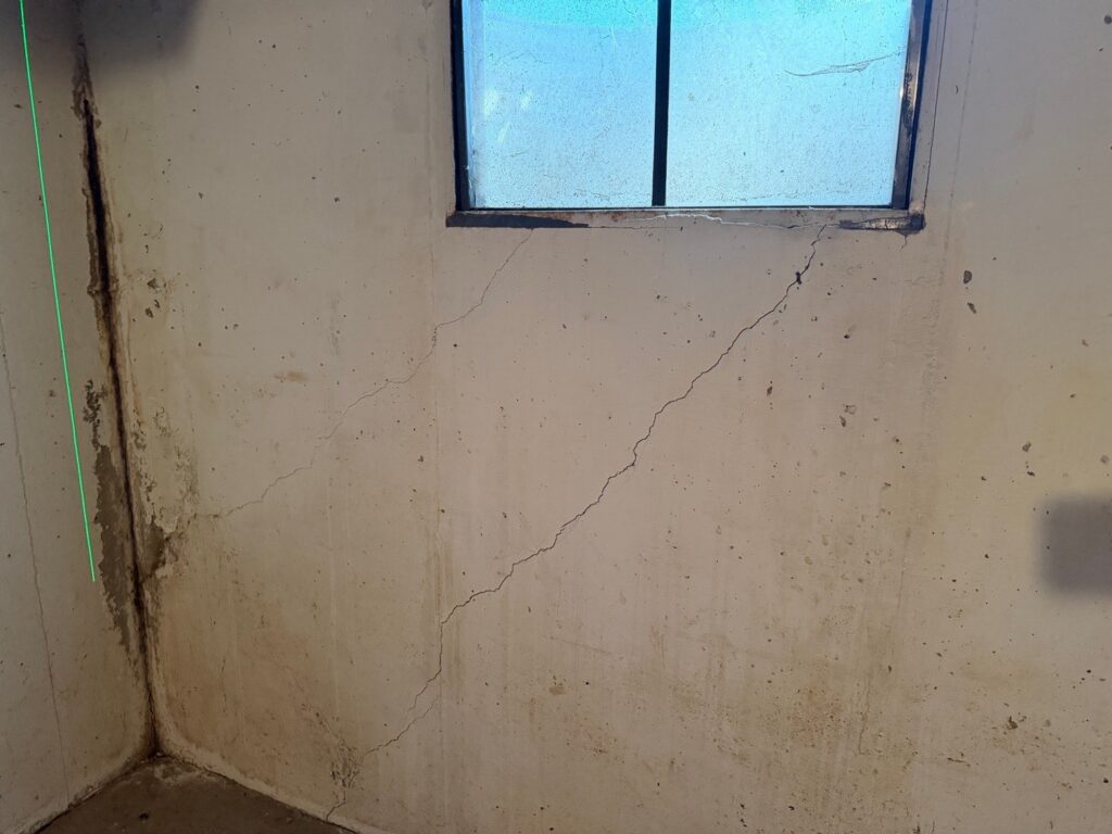 Diagonal cracks running down from the corners of a basement window in a concrete foundation wall, found during a home inspection in Leawood, KS