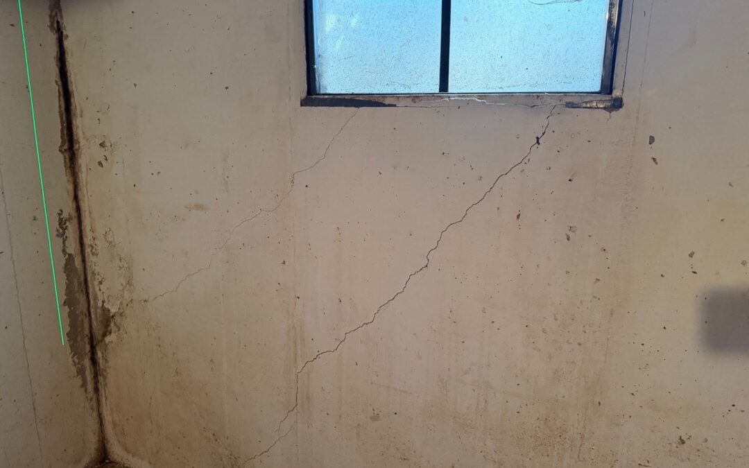 Diagonal cracks running down from the corners of a basement window in a concrete foundation wall, found during a home inspection in Leawood, KS