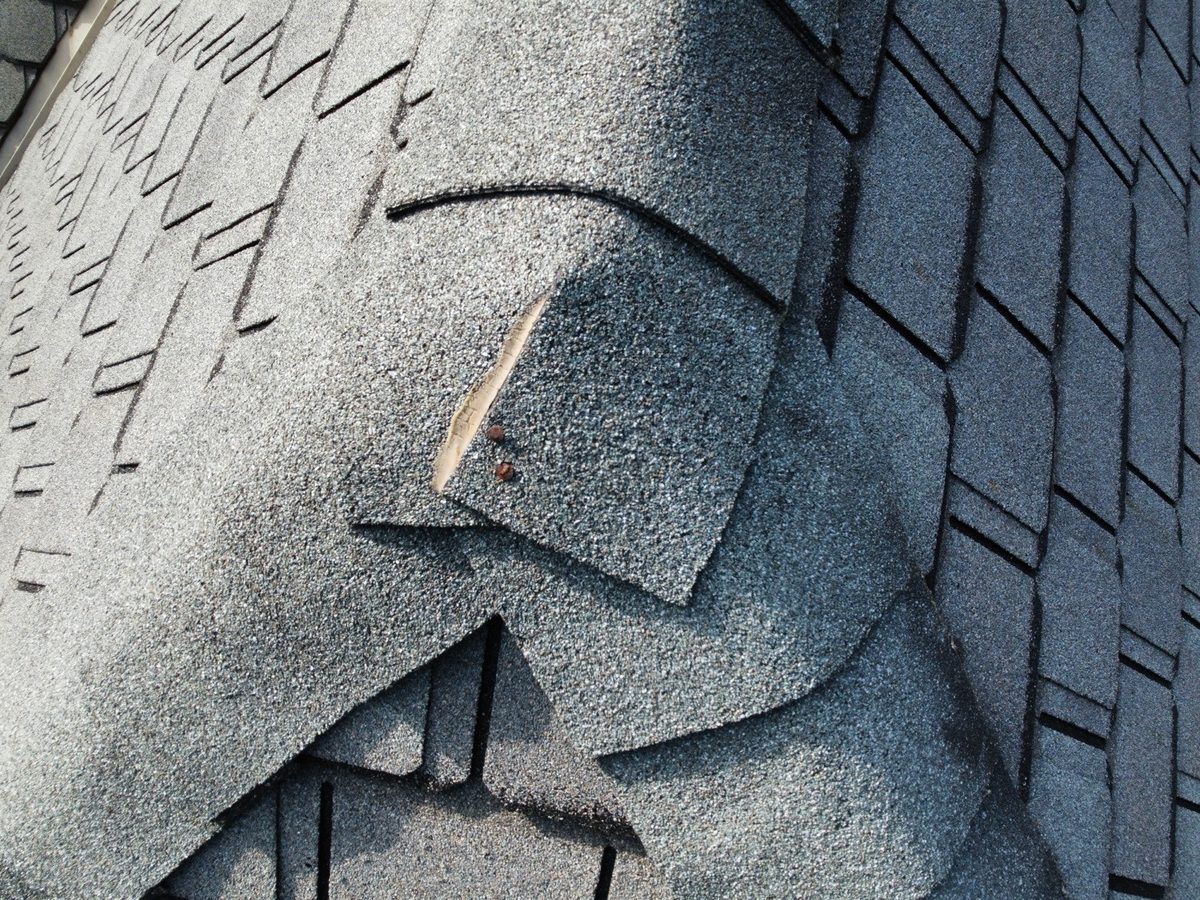 Cracked hip shingle with exposed nail heads on a roof found during a home inspection in Liberty, MO