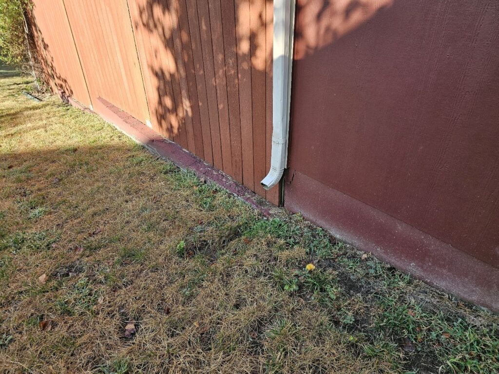 Downspout ending at the base of a house's siding with no extension, found during a home inspection in Olathe, KS