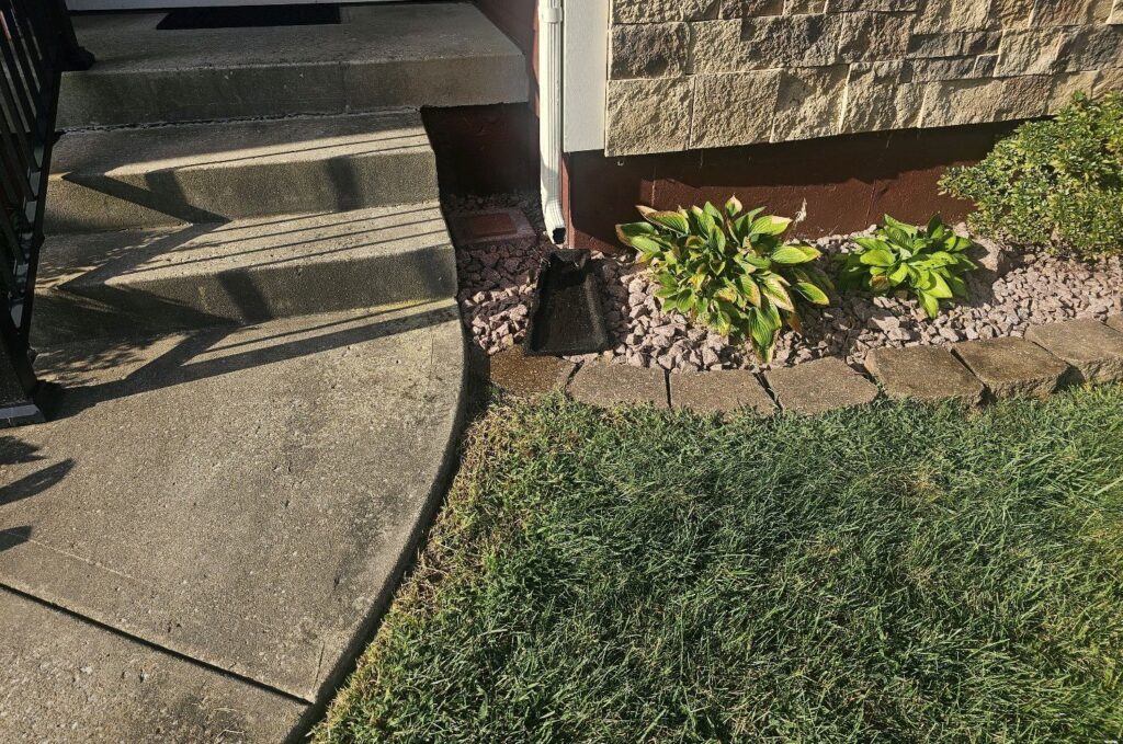 Downspout emptying onto a short splash block in a rock bed beside an entry step, found during a home inspection in Olathe, KS