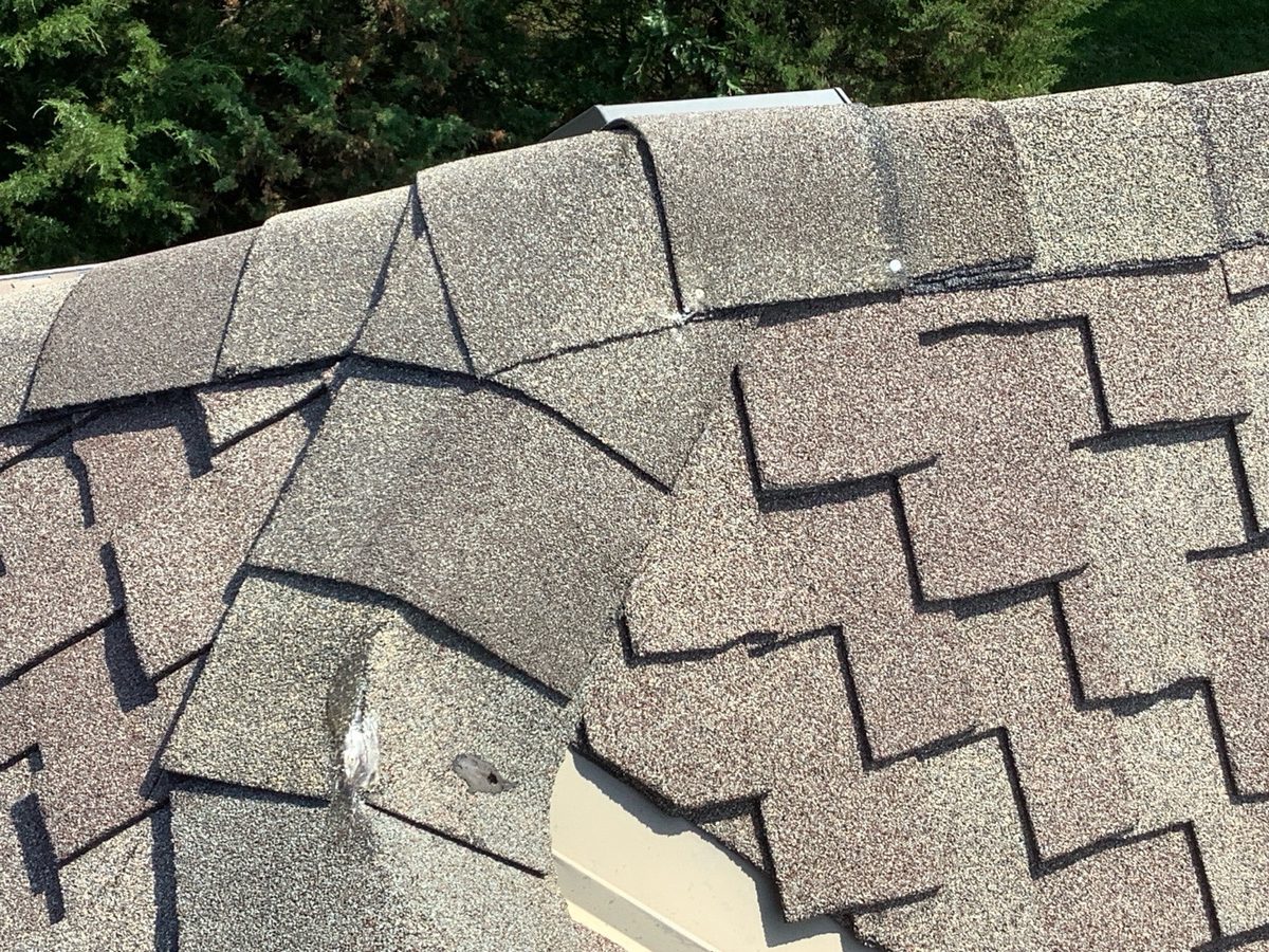 Lifted and damaged ridge shingles with exposed nails on the roof found during a home inspection in Parkville, MO