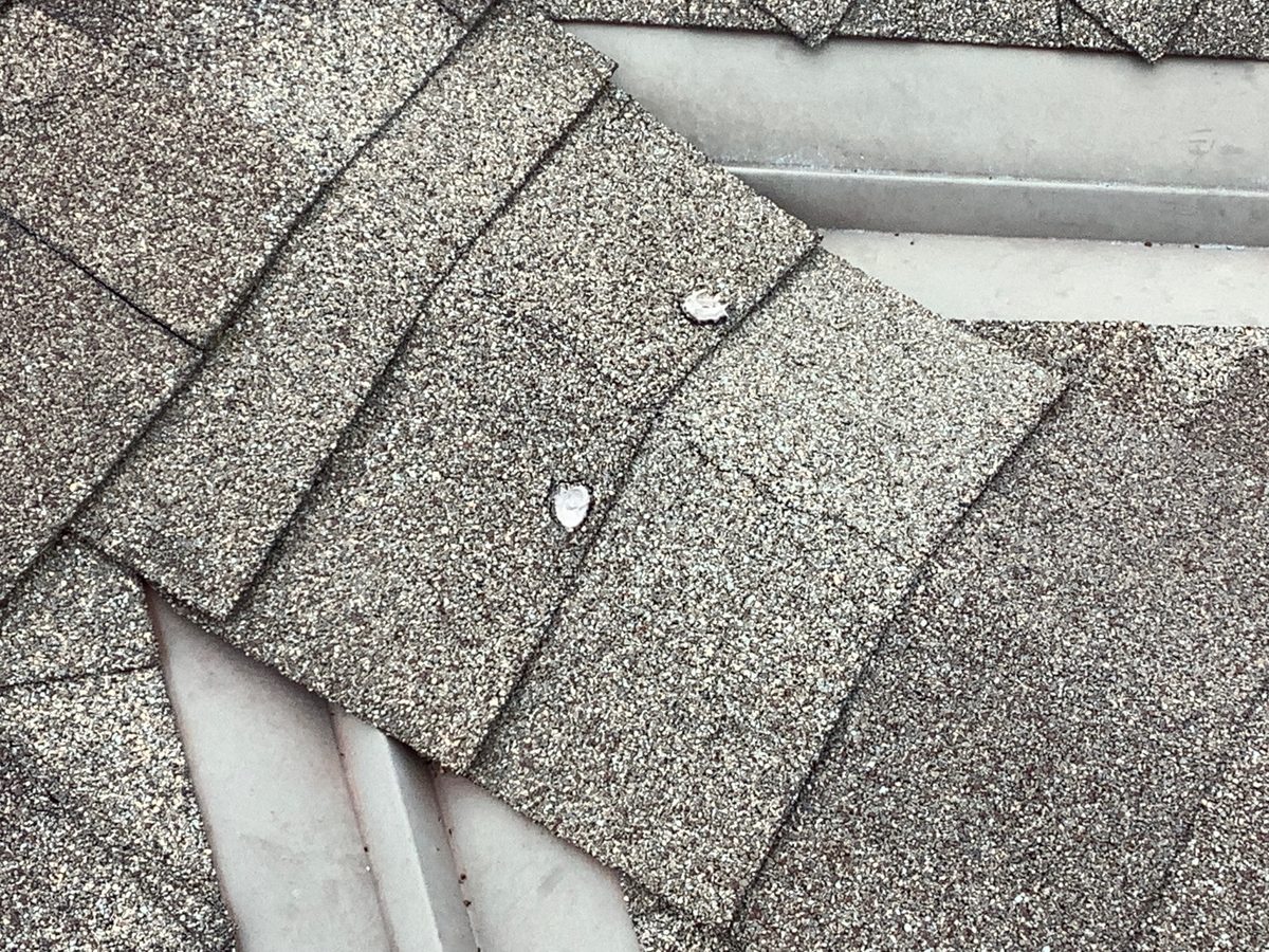 Exposed nail heads on asphalt shingles beside a metal roof valley found during a home inspection in Raytown, MO